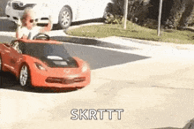 a young boy is driving a red toy car on a street .