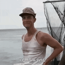 a man wearing a hat and a tank top is standing in front of a fishing net and talking about a wig .