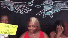a woman is holding a sign that says `` washed up hunnie '' in front of a chalkboard .
