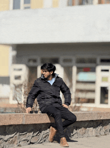 a man wearing a black jacket sits on a stone wall