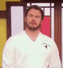 a man in a white karate uniform is standing in front of a window with his eyes closed .
