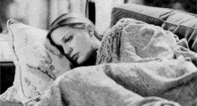 a black and white photo of a woman laying on a couch under a blanket .