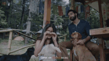 a man and a woman are petting their dogs while a now streaming advertisement is displayed