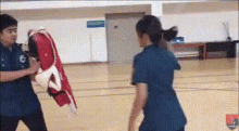 a man and a woman are fighting in a gym . the woman is wearing a blue scrub top .