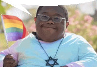 a man wearing glasses and a star necklace is holding a small rainbow flag