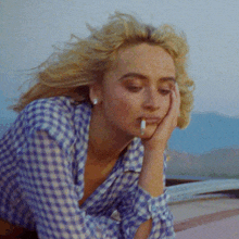 a woman with a cigarette in her mouth is wearing a plaid shirt