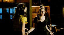 two women are holding hands in a dark room and one is wearing a yellow shirt