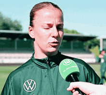 a woman wearing a vw jacket is being interviewed with a green microphone