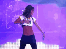 a woman in a crop top is dancing on a stage in front of a purple background with the word erdose at the bottom