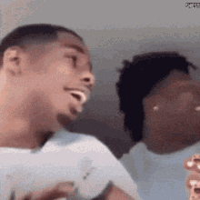a man in a white shirt is laughing while another man is eating popcorn