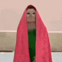 a doll is wrapped in a pink towel and standing in front of a wall .