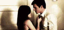 a man and a woman are kissing in front of a door . the woman is pulling the man 's tie .