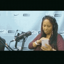 a woman wearing headphones looks at her phone in front of a microphone at radio city