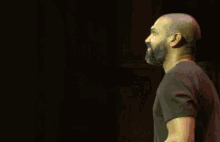 a bald man with a beard is raising his hand in the dark