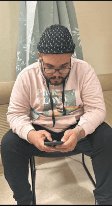 a man wearing a pink floyd sweatshirt sits on a chair looking at his phone