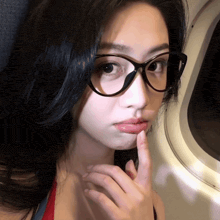a woman wearing glasses has her finger to her mouth