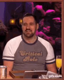 a man wearing a shirt that says critical role is sitting at a table .