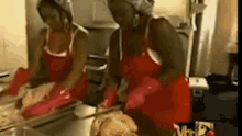 two women wearing red aprons and gloves are cleaning a chicken in a kitchen .
