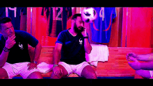 a man with a beard holds a soccer ball on his head in a locker room