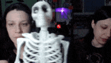 two women are standing next to a skeleton with a purple light in the background