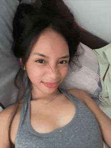a woman in a grey tank top is laying on a bed and smiling