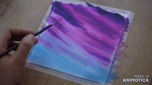 a person is painting a purple and blue sky with a brush .