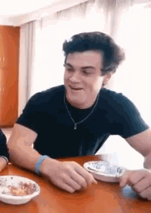 a young man is sitting at a table with a bowl of food and a bowl of cereal .