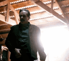 a man with a mustache is standing in a dark room with a light coming from the ceiling .