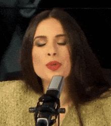 a woman singing into a microphone with her eyes closed and red lips