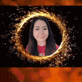 a woman in a red shirt is smiling in front of a circle of fire .