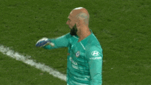 a man with a beard is standing on a soccer field wearing a blue jersey .