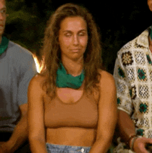 a woman in a crop top with a green scarf around her neck is sitting in a group of people .