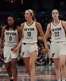three female basketball players wearing fever jerseys walk on the court