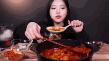 a woman is eating food from a pot with chopsticks and a spoon .