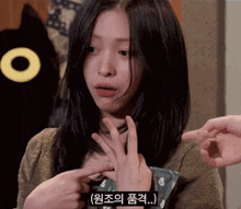 a woman in a brown sweater is pointing at her hand with a foreign language subtitle
