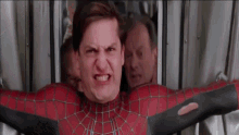 a man in a spiderman costume is making a funny face while standing in front of a wall .
