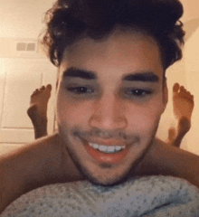 a man is smiling while laying on a bed with his feet up .