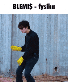 a man in a black shirt and yellow gloves is dancing in front of a wall that says blemi $ - fysika