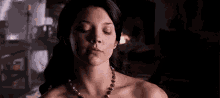 a woman without a shirt is wearing a necklace with her eyes closed in a dark room .