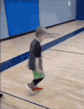a young boy is jumping on a wooden basketball court .