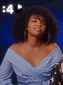a woman with curly hair is wearing hoop earrings and a blue striped shirt with the number 4 behind her