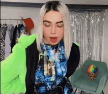 a woman wearing a blue shirt and a green jacket is standing in front of a chair with a stuffed animal on it .