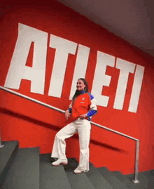 a woman is standing on a set of stairs in front of a wall with the word atleti on it