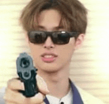 a young man wearing sunglasses and a suit is pointing a gun at the camera .