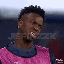 a man with a mohawk is making a funny face while wearing a pink shirt and a blue shirt .