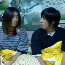 a man and a woman are sitting next to each other in front of a wall with a picture of a guitar on it .