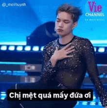 a man in a sheer shirt is holding his hand to his chest while standing on a stage .