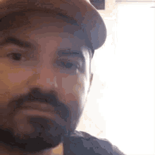 a man with a beard is wearing a baseball cap and making a funny face .