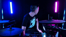 a man in a black shirt is playing drums in a dark room