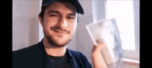 a man with a beard is smiling while holding a piece of paper in front of a window .